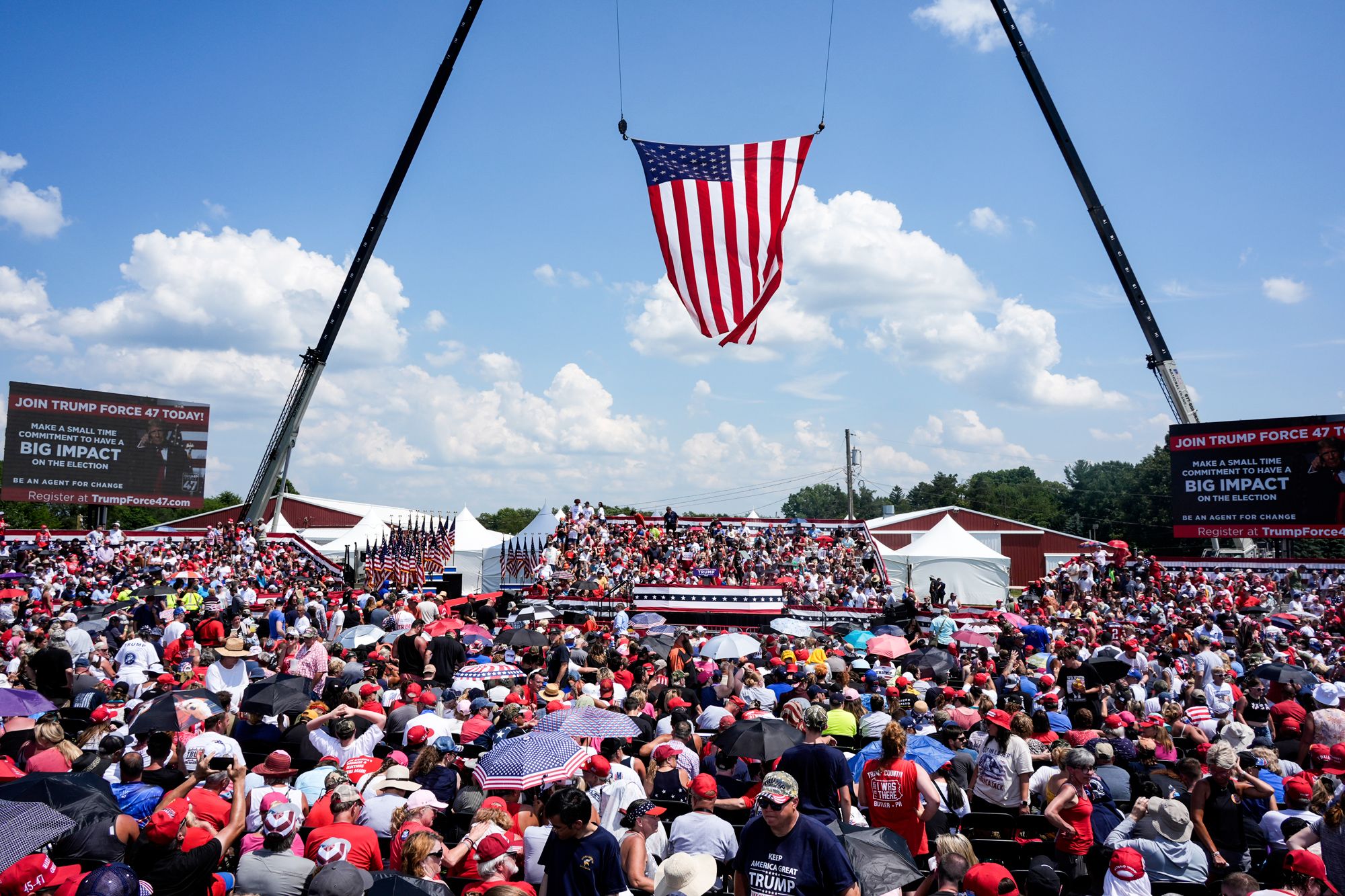 A large crowd outside at a rally, an American flag hangs overhead